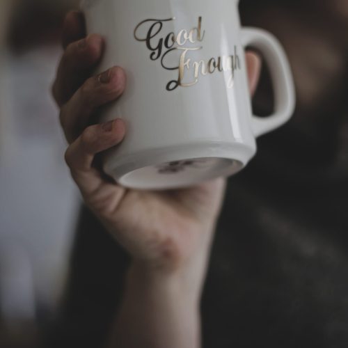 hand-holding-a-white-mug-with-gold-cursive-lettering-good-enough-perfectionism-anxiety-counselling-kelowna-alive-counselling-barb-egan